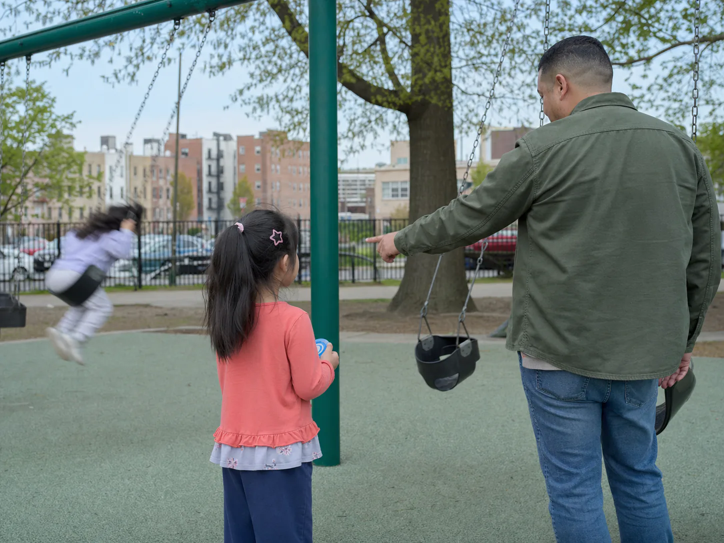 Niña esperando su turno en el columpio del parque con apoyo cerca